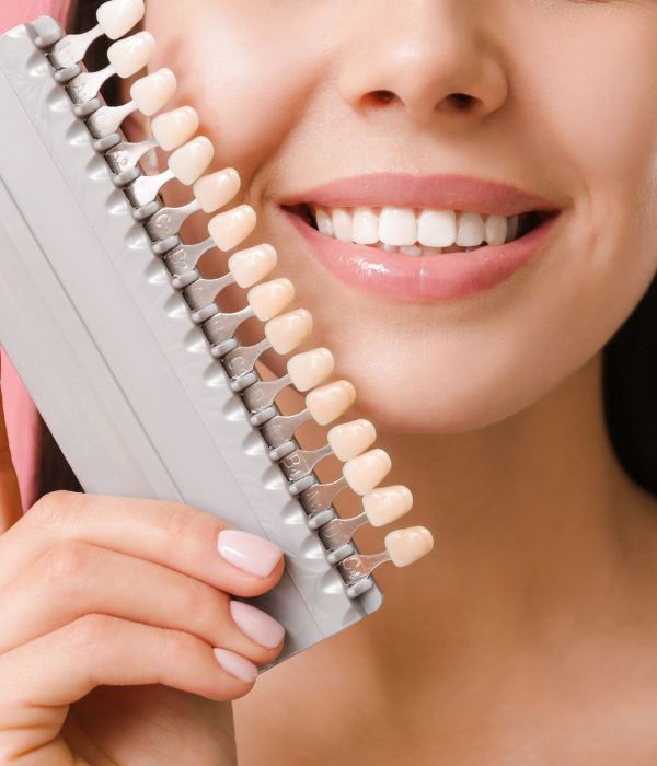 Porcelain Veneers A woman holding a tooth shade chart smiling.